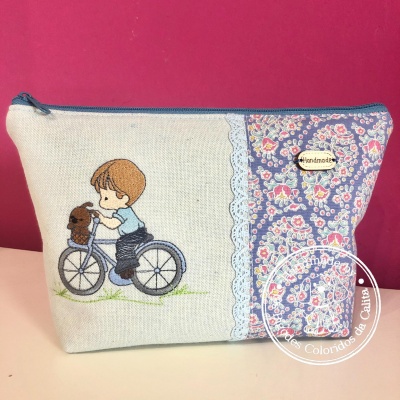 Necessaire de tecido com fecho azul, bordado de criança numa bicicleta com cão e padrão floral azul colorido
