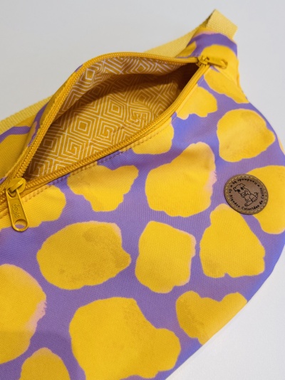 Bolsa tipo cintura amarela e lilás com padrão e fecho amarelo aberta mostrando interior geométrico