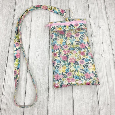 Bolsa pequena floral com fecho rosa e alça comprida sobre madeira clara