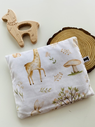 Almofada pequena estampada com desenhos de animais e plantas junto com brinquedo de madeira em formato de lhama.