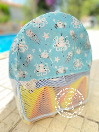 Bolsa azul com padrão marinho, bolso de rede e objetos coloridos junto a piscina