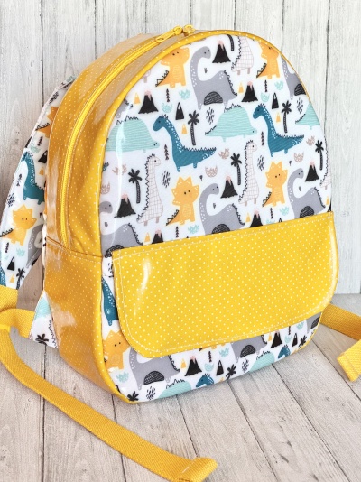 Mochila infantil com padrão de dinossauros em tons azul, amarelo e cinza com bolso amarelo de bolinhas brancas