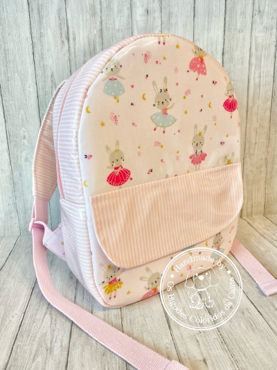 Mochila infantil rosa com padrão de coelhinhos bailarinas e bolso frontal listrado