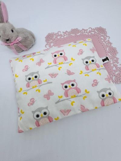 Almofada branca com padrão de corujas e borboletas, tapete rosa e peluche coelho cinzento