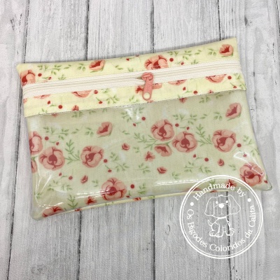 Estojo floral creme e vermelho com fecho rosa sobre madeira clara