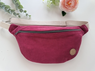 Bolsa pochete vermelho-vinho em veludo cotelê com fecho e cinto bege, decorada com botão redondo castanho, sobre fundo branco com flores.