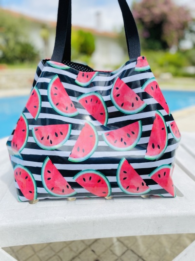 Mala com padrão de melancias e alças pretas numa mesa junto a piscina