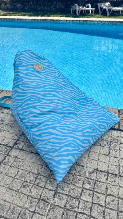 Almofada azul com padrão listrado junto à piscina e piso de mosaico