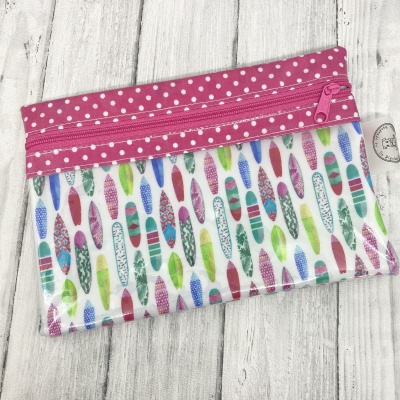 Estojo colorido com padrão de pranchas de surf e fecho rosa com bolinhas brancas