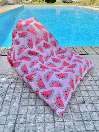 Almofada estampada rosa com melancias ao lado de uma piscina azul