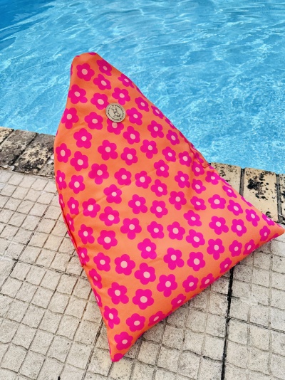 Almofada laranja com flores cor-de-rosa junto a piscina com ladrilhos