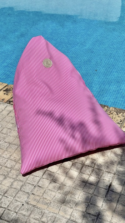 Pufe triangular riscado rosa e branco ao lado de piscina em pavimento de pedra