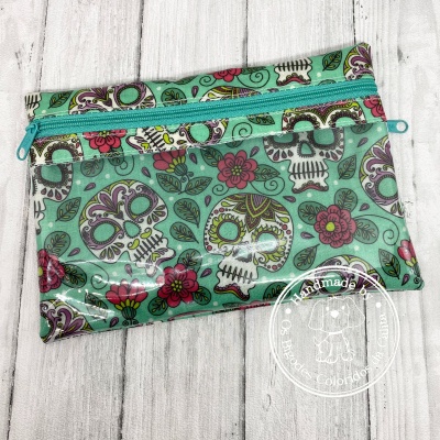 Bolsa impermeável com padrão de caveiras e flores verdes e fecho azul