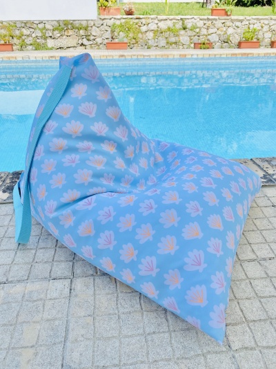Puff triangular azul claro com padrão floral ao lado de piscina