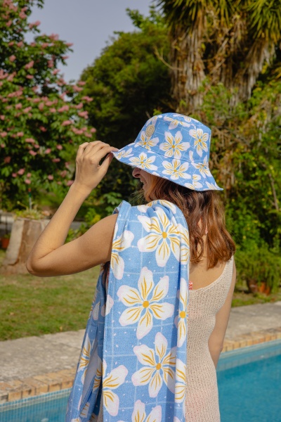 Chapéu e toalha de praia azuis com flores brancas e amarelas usados por pessoa junto a piscina
