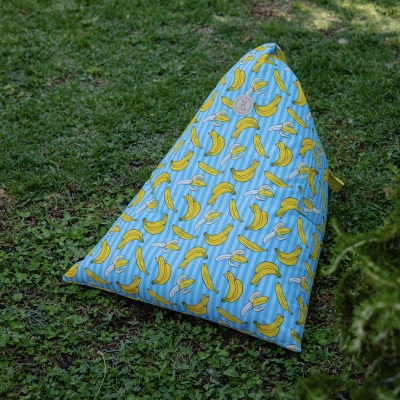 Pufe com padrão de bananas sobre fundo azul, colocado na relva