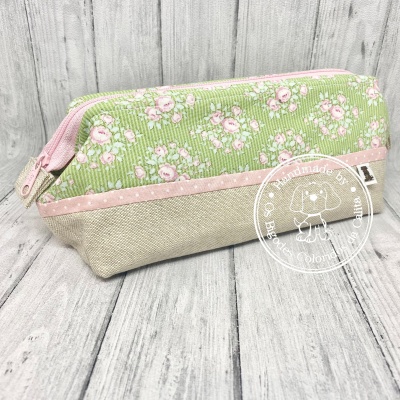 Estojo pequeno floral verde e rosa com fecho de correr rosa sobre madeira clara