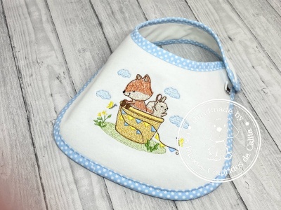Babete branco com borda azul polka dots e bordado colorido de animais num balde amarelo