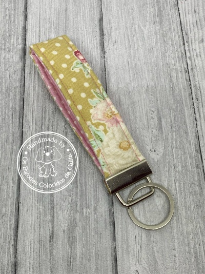 Chaveiro tecido floral amarelo e rosa com argola metálica sobre fundo de madeira cinza