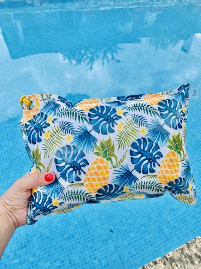 Bolsa de tecido colorida com padrão de folhas e ananases segurada junto a piscina.
