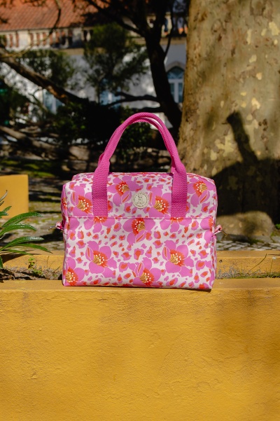 Mala rosa com padrão floral colocada sobre estrutura amarela ao ar livre