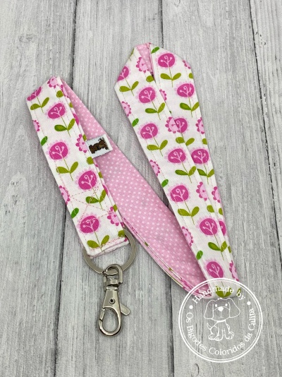 Fita floral rosa e verde com gancho metálico e selo artesanal em fundo de madeira