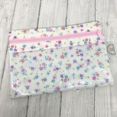 Estojo transparente com padrão floral colorido e fecho rosa sobre madeira clara