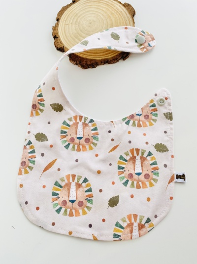 Babete de tecido branco com padrão colorido de leões e folhas