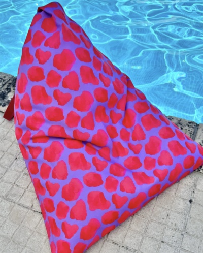 Pufe triangular com padrão de manchas vermelhas e fundo lilás junto a piscina