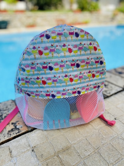 Mochila pequena colorida com padrão de gelados e bolso em malha com pás de praia junto a piscina