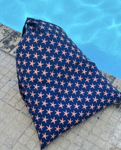 Pufe azul escuro com estrelas cor-de-rosa junto a uma piscina.