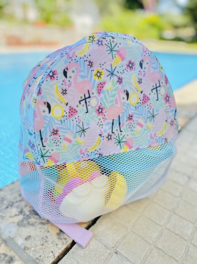 mochila infantil azul claro com flamingos cor-de-rosa e bolso em rede branco ao lado de piscina
