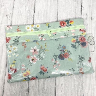 Necessaire floral plastificada com fecho verde claro sobre superfície de madeira clara