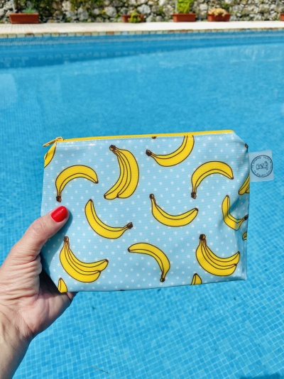 Necessaire azul claro com bananas amarelas segurada em frente a uma piscina.