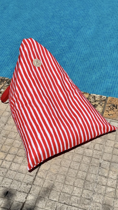 Pufe riscado vermelho e branco ao lado de piscina com azulejos azuis