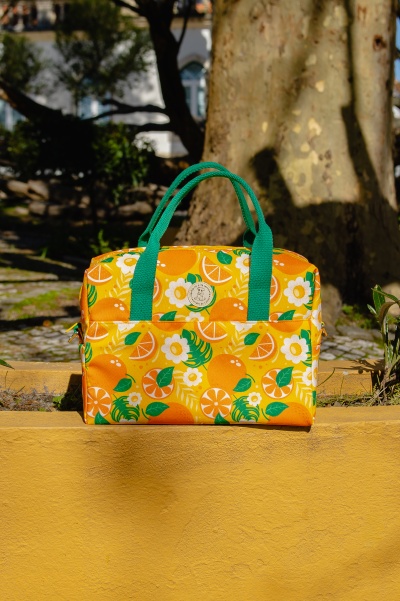 Mala de mão amarela com padrão laranja e verde apoiada num muro amarelo ao ar livre