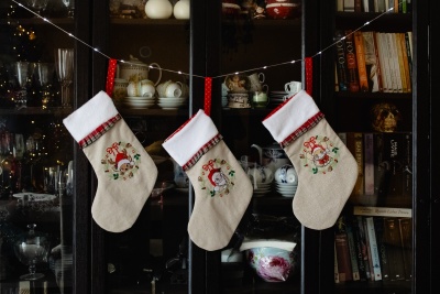 Três meias de Natal bordadas penduradas em móvel com louças e livros ao fundo