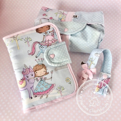 Conjunto de artigos infantis em tecido com padrão de princesas e unicórnios em tons pastel.
