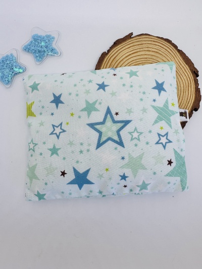 Almofada decorativa branca com estrelas coloridas sobre fundo branco com tronco de madeira e estrelas decorativas
