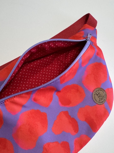 Bolsa pochete lilás com manchas vermelhas, fecho lilás e interior vermelho com pontos brancos