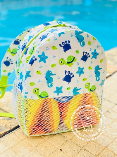Mochila infantil colorida com desenhos marinhos junto à piscina