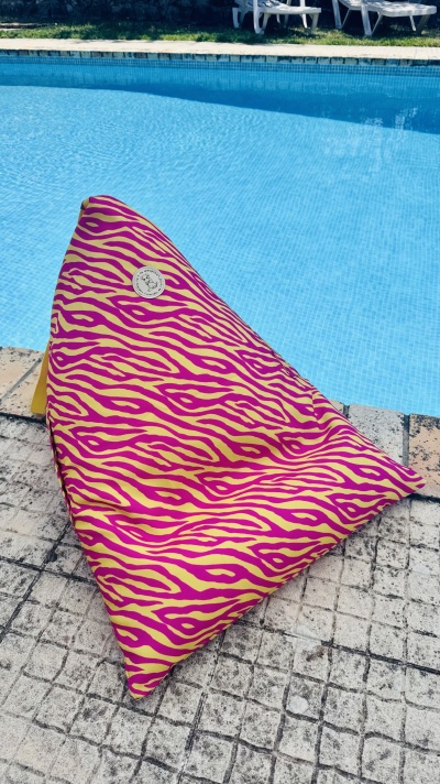 Puff triangular zebrado amarelo e rosa junto a piscina