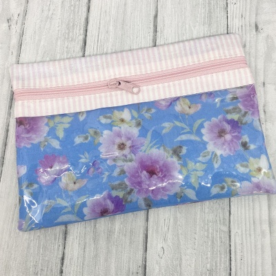 Necessaire floral azul e rosa com fecho de correr rosa sobre fundo de madeira branca