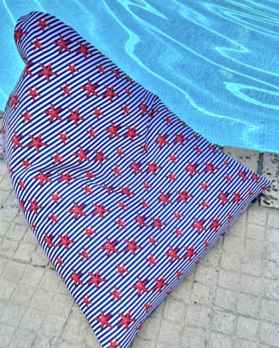 Colchão insuflável listrado azul e branco com estrelas vermelhas ao lado de uma piscina