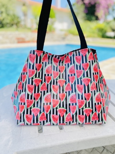 Mala estampada com fatias de melancia e riscas pretas e brancas junto a uma piscina