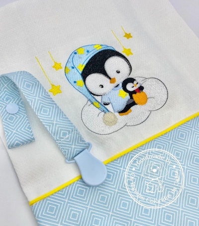 Fralda de tecido branco com bordado de pinguins e detalhe azul com padrão geométrico.