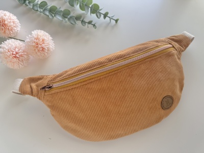 Pochete castanha em veludo cotelê com fecho éclair bege em fundo branco com flores e folhagem.