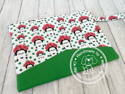 Bolsa de tecido branca com padrão de rostos femininos e flores vermelhas, parte inferior verde com selo 'Handmade by Os Bigodes Coloridos da Cátia'