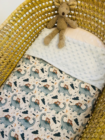 Cobertor para bebé com padrão de dinossauros e ursinho de peluche num berço de vime amarelo