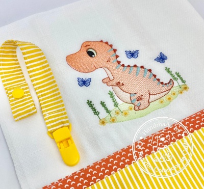 Pano de bebé com bordado de dinossauro e fita amarela com clip
